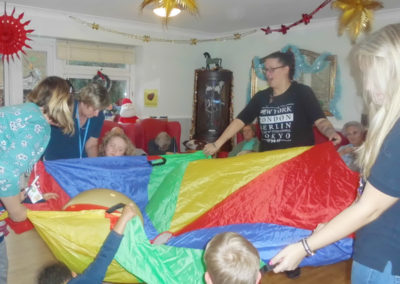 Young children from Rodmersham Nursery playing parachute games with residents from Woodstock Residential Care Home