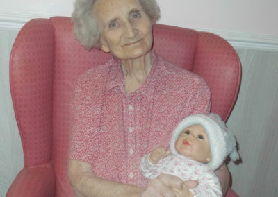 A smiling female Woodstock resident with a doll being used for Doll Therapy