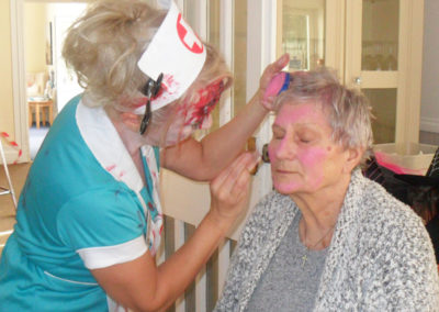 Staff painting a resident's face with pink Halloween face paints