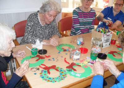 Residents at a table making paper Christmas wreath decorations at Woodstock Residential Care Home