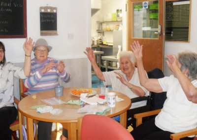 Residents at Woodstock smiling and waving their hands around a table