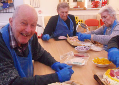 Residents smiling and creating their own pizzas around a table at Woodstock