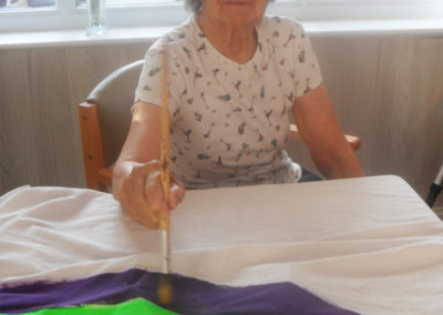 Lady resident at Woodstock Residential Care Home painting a giant rainbow on a sheet