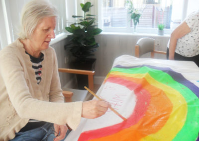 Lady resident painting a giant rainbow on a sheet at Woodstock Residential Care Home