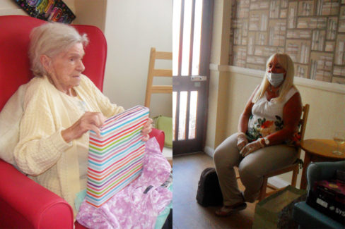 Resident opening a birthday gift and her daughter visiting at a distance